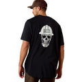 Man wearing a black t-shirt with a skull and hard hat graphic on the back, standing against a white background.