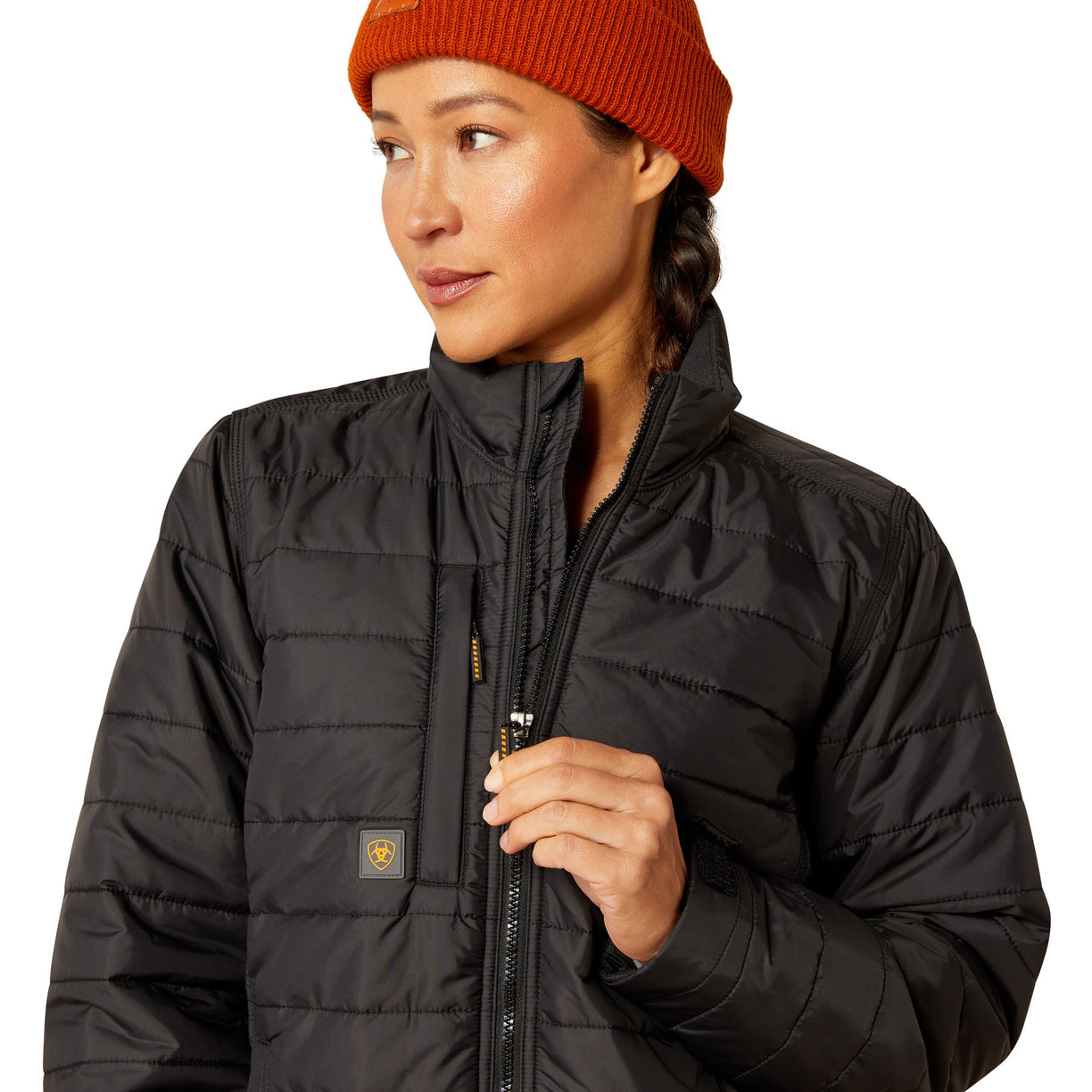 Person wearing a black puffer jacket and orange beanie on a white background