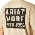 Man wearing a beige t-shirt with 'Ariat Work Est. 1993' print on the back, on a white background