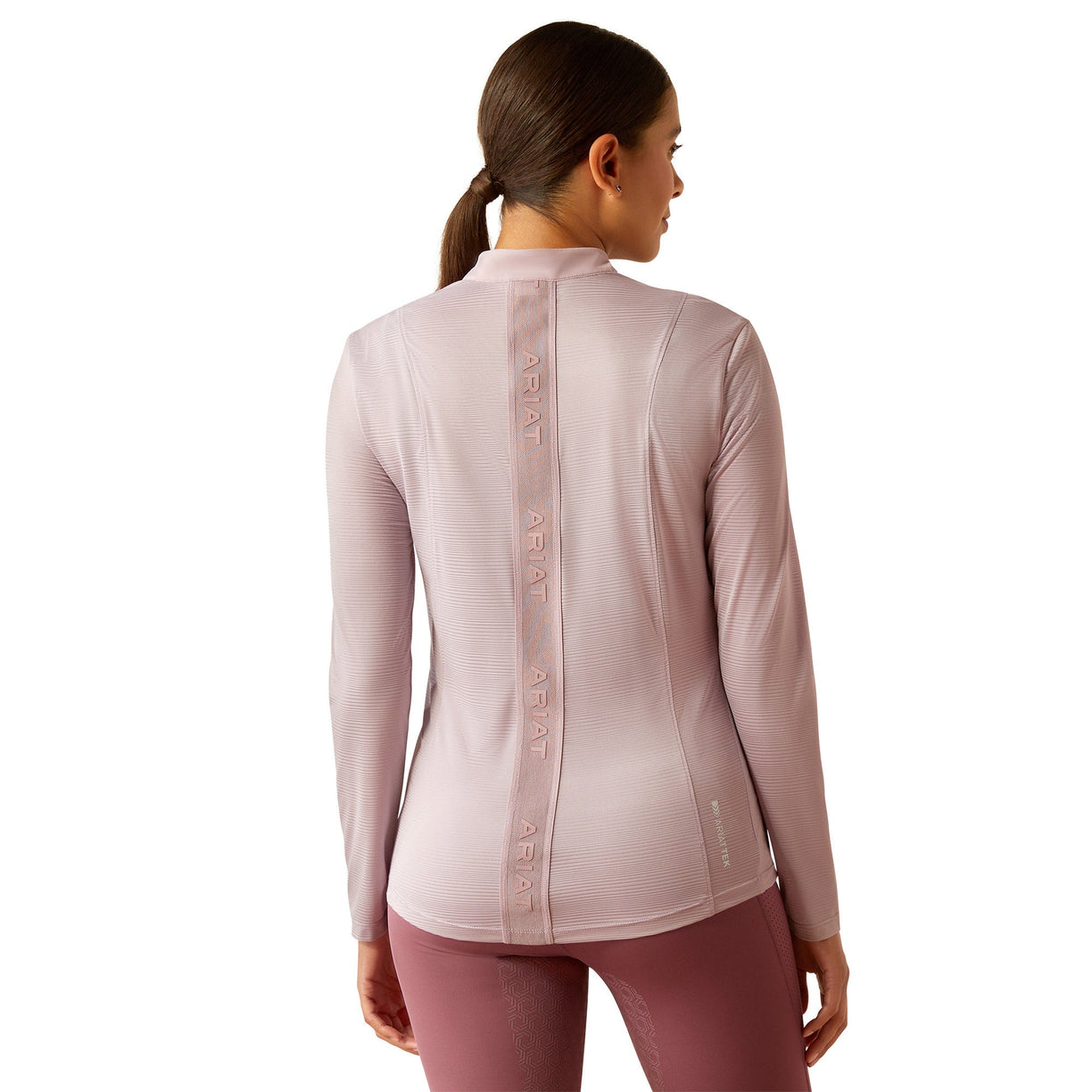 Woman wearing a light pink long-sleeve athletic top with 'Ariat' branding on a white background