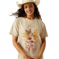 Woman wearing a beige t-shirt with floral and deer design, blue jeans, and a cowboy hat on a white background