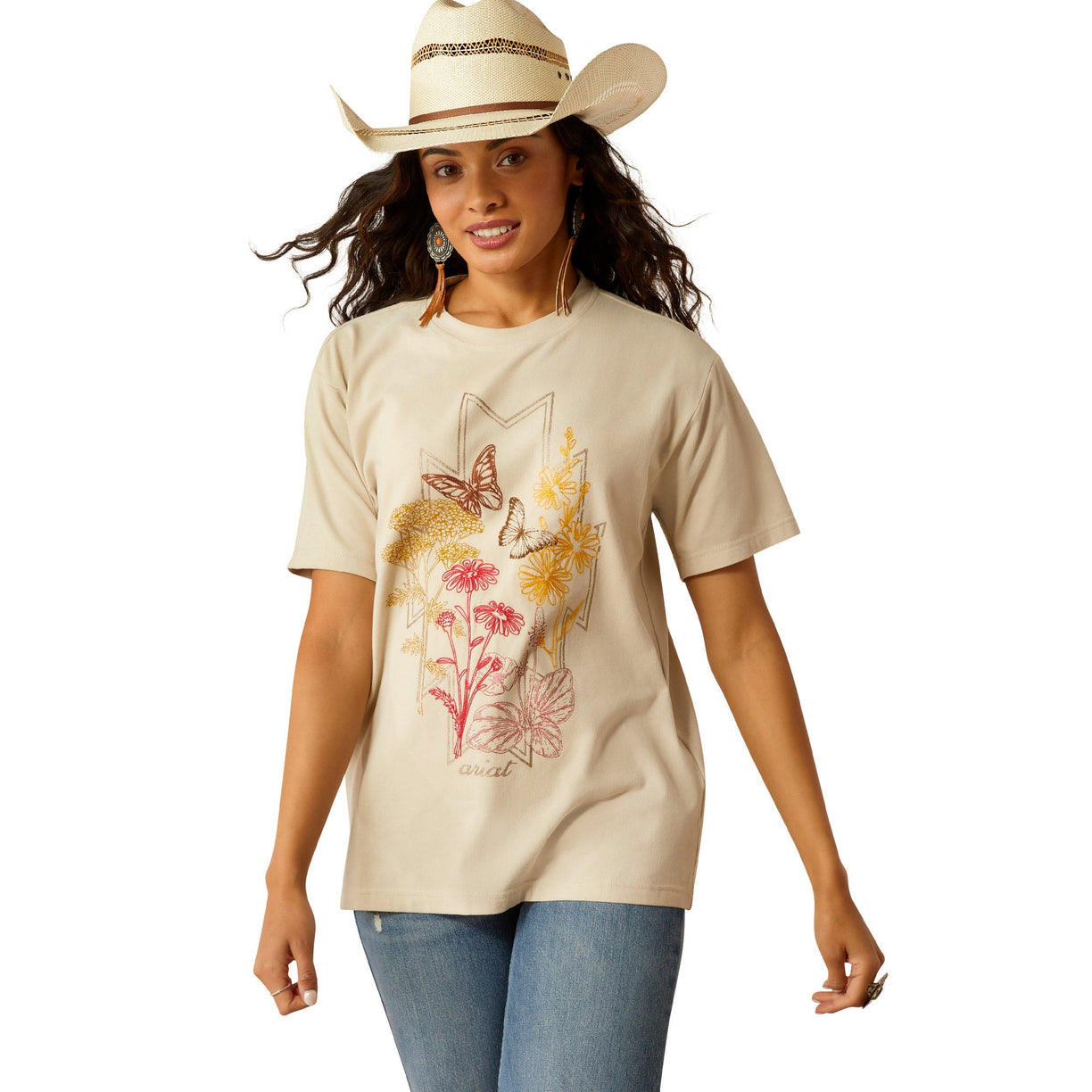 Woman wearing a beige t-shirt with floral and deer design, blue jeans, and a cowboy hat on a white background