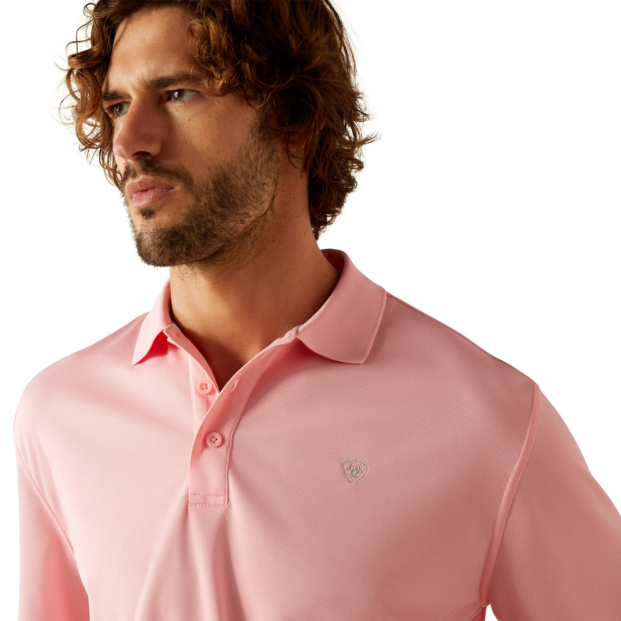 Man wearing a pink polo shirt with Ariat branding on a white background