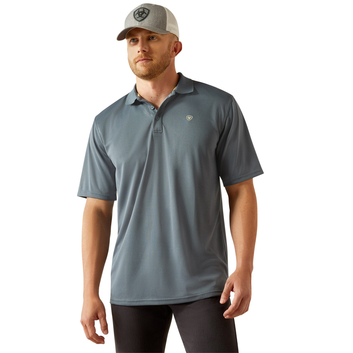 Man wearing a blue gray polo shirt with Ariat branding and cap on a white background