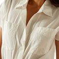 Close-up of a person wearing a light beige button-up shirt on a white background