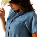 Woman wearing a blue denim shirt holding a straw hat against a white background