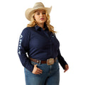 Woman wearing a navy Ariat shirt, jeans, and a cowboy hat on a white background