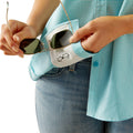 Person holding sunglasses over a white pouch with a sunglasses icon, wearing a blue checkered shirt and jeans.