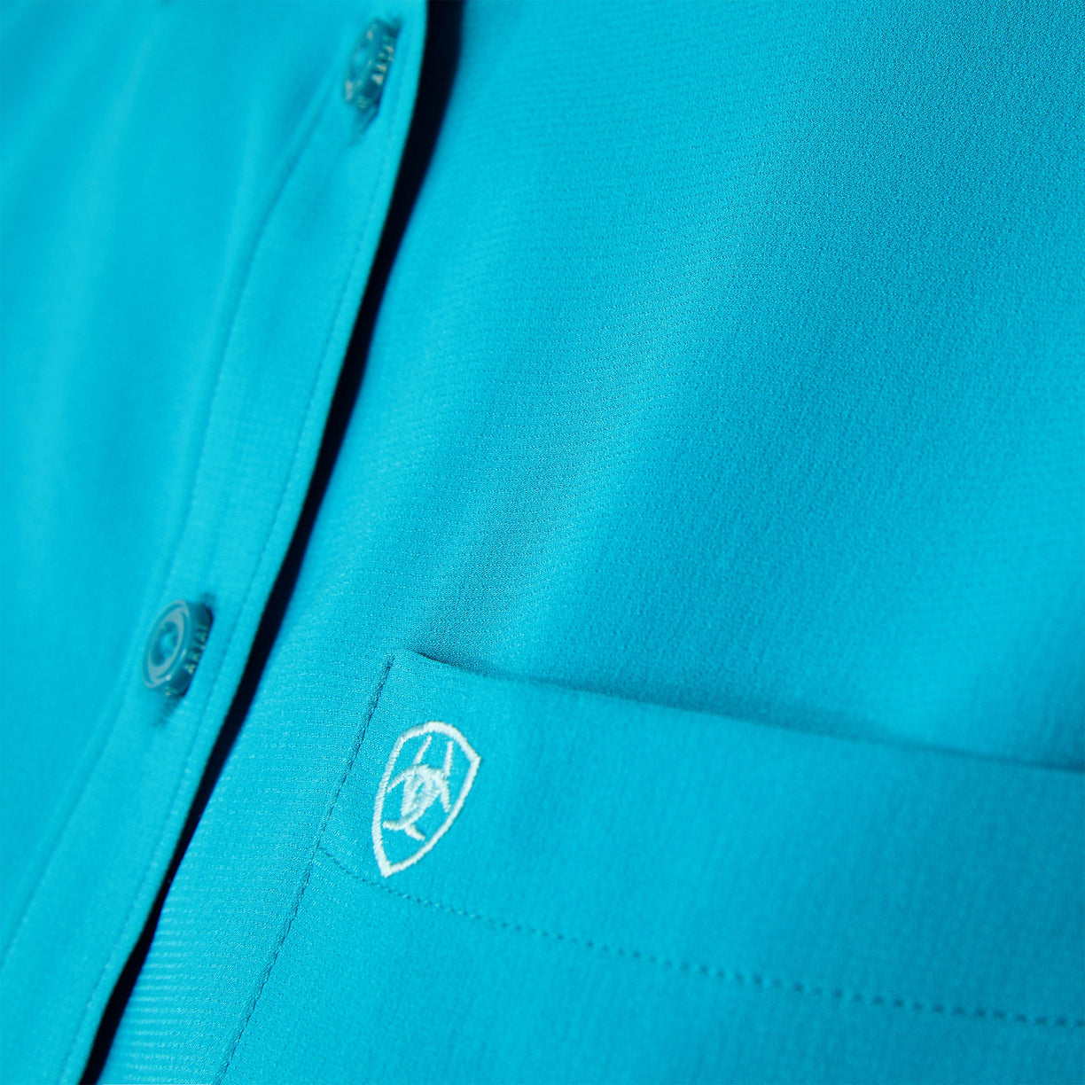 Close-up of a blue shirt with a logo on the chest pocket.