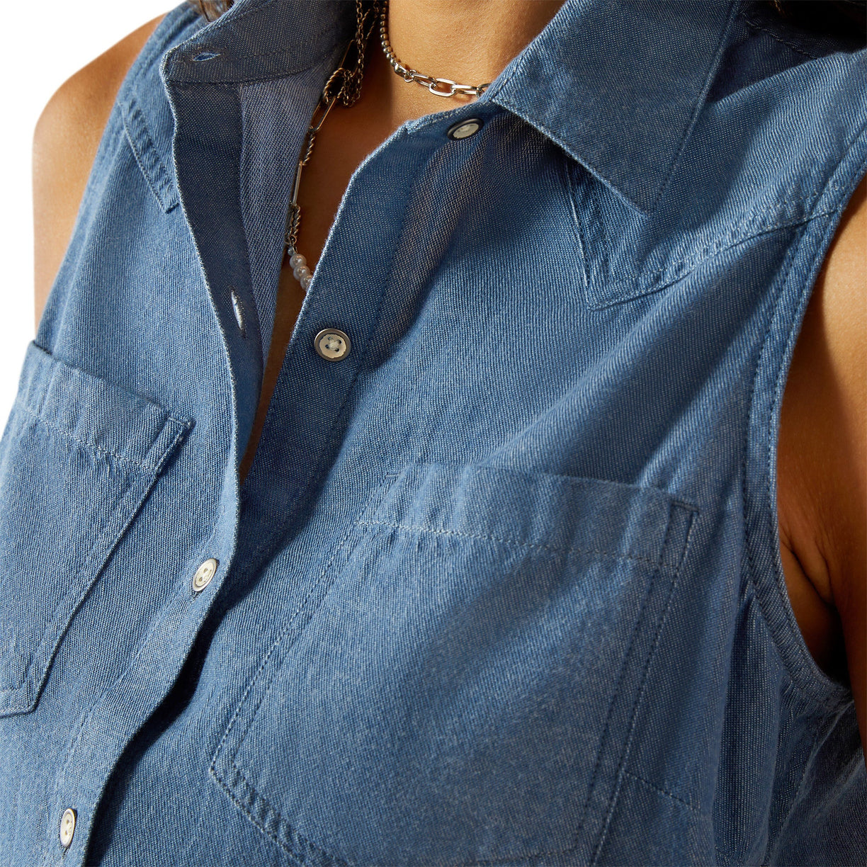 Woman wearing a blue sleeveless denim top and light blue denim on a white background