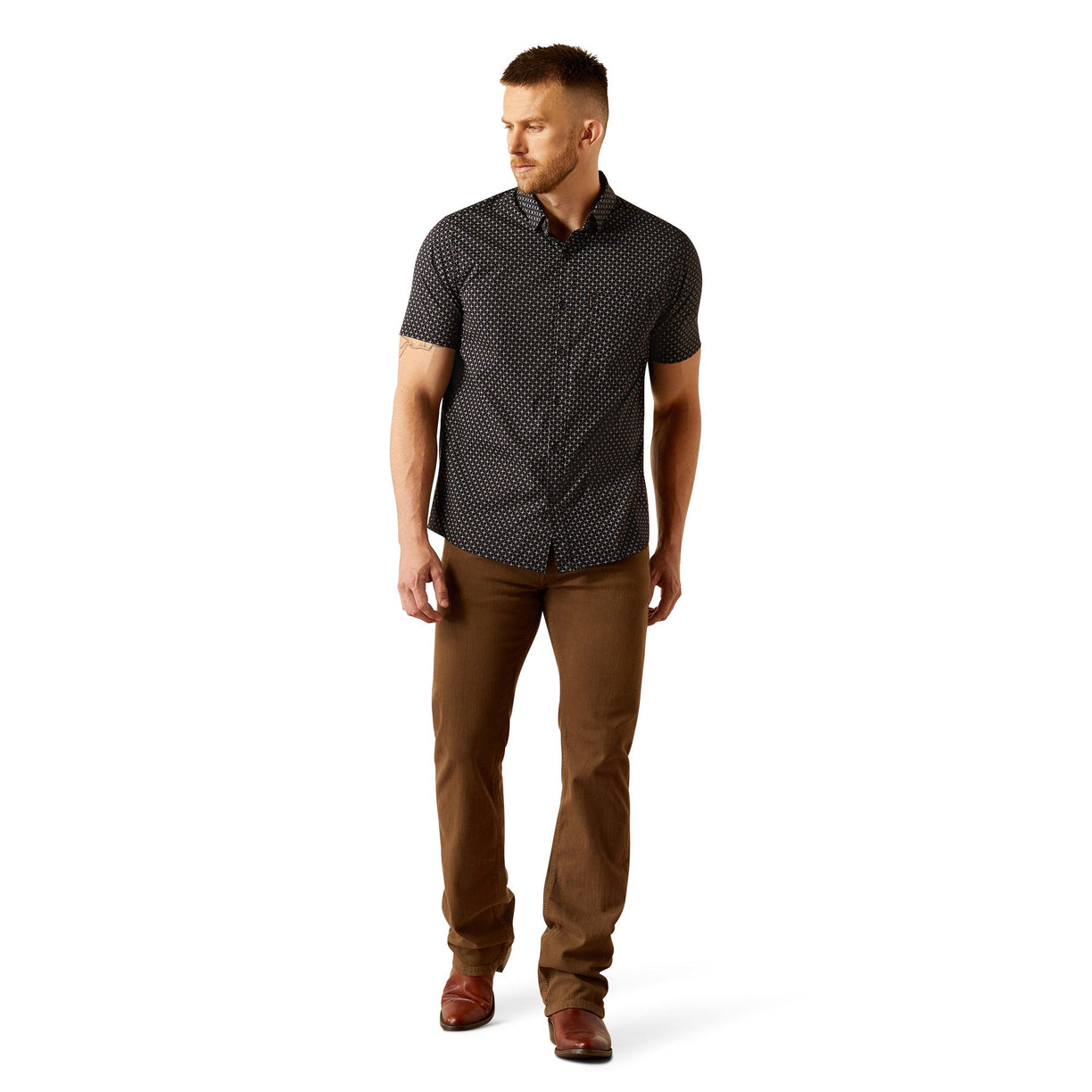 Man wearing a patterned black shirt and brown pants on a white background