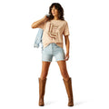 Woman wearing a beige t-shirt, light blue shorts, and brown cowboy boots on a white background