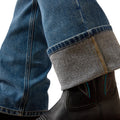 Close-up of blue jeans with gray cuffs and black leather boots on a white background