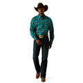 Man wearing a turquoise plaid shirt, dark jeans, and a brown cowboy hat on a white background