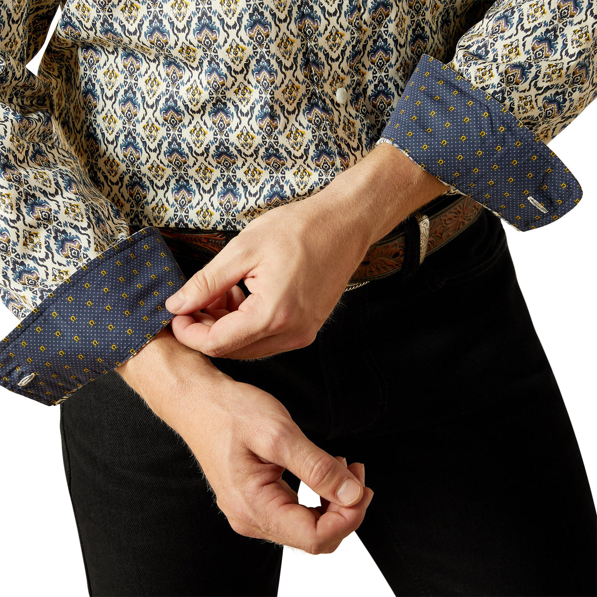 Person adjusting the cuff of a patterned shirt with a white background