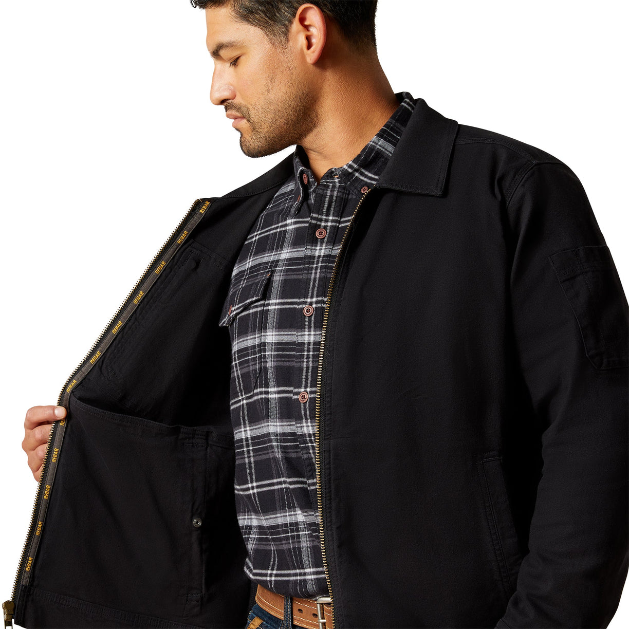 Man wearing a black jacket over a plaid shirt on a white background