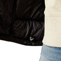 Close-up of a black puffer jacket with a beige sweater and blue jeans on a white background