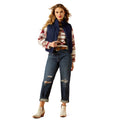 Woman wearing a patterned sweater, blue vest, and jeans on a white background