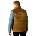 Man wearing a brown quilted vest over a denim jacket on a white background