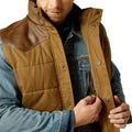 Man wearing a brown quilted vest over a denim jacket on a white background