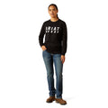 Person wearing a black Ariat sweatshirt and blue jeans on a white background