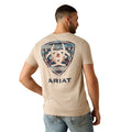 Man wearing a beige t-shirt with a geometric design and 'Ariat' branding on the back.