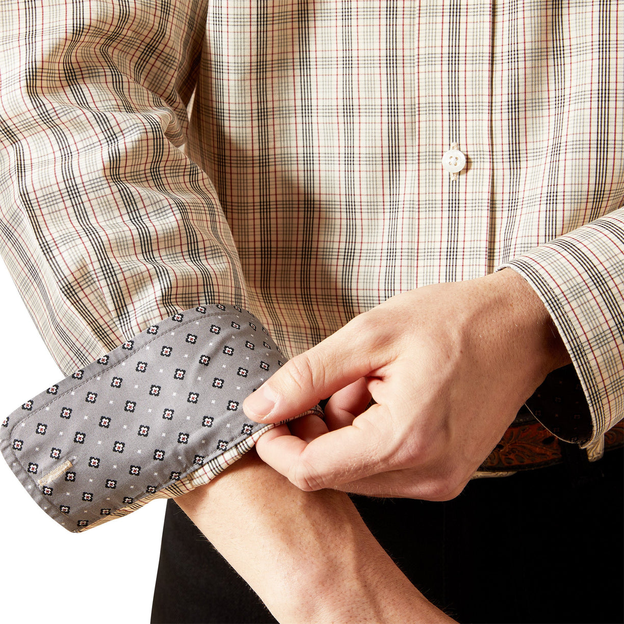 Person rolling up the sleeve of a plaid shirt with a patterned cuff.