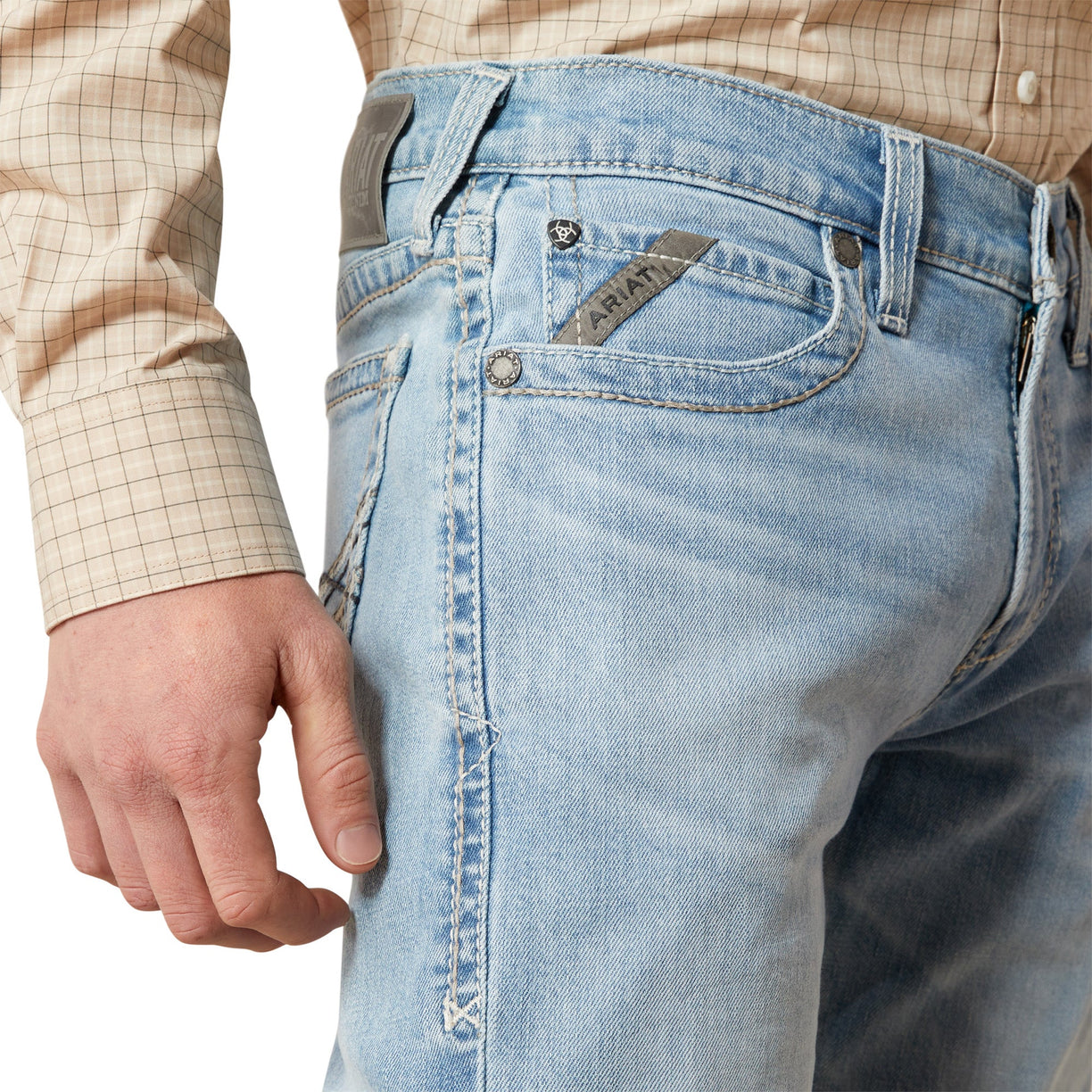 Close-up of light blue jeans with a brand logo, worn by a person.