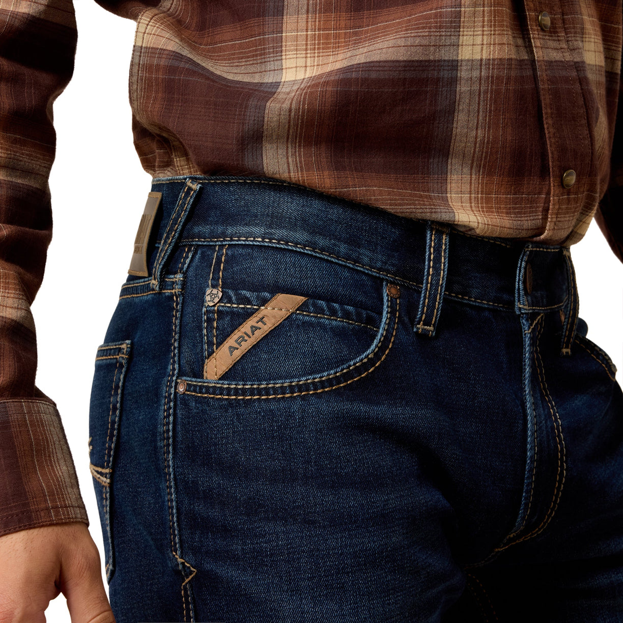 Person wearing blue jeans with Ariat logo, brown plaid shirt on a white background
