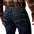 Person wearing blue jeans with Ariat logo on a white background