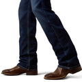 Dark blue jeans worn by a person with brown shoes on a white background