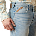 Close-up of a person wearing light blue jeans with a visible Ariat brand label.