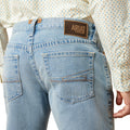 Light blue jeans with Ariat logo on the back pocket against a neutral background