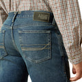 Person wearing blue jeans with Ariat logo on a white background