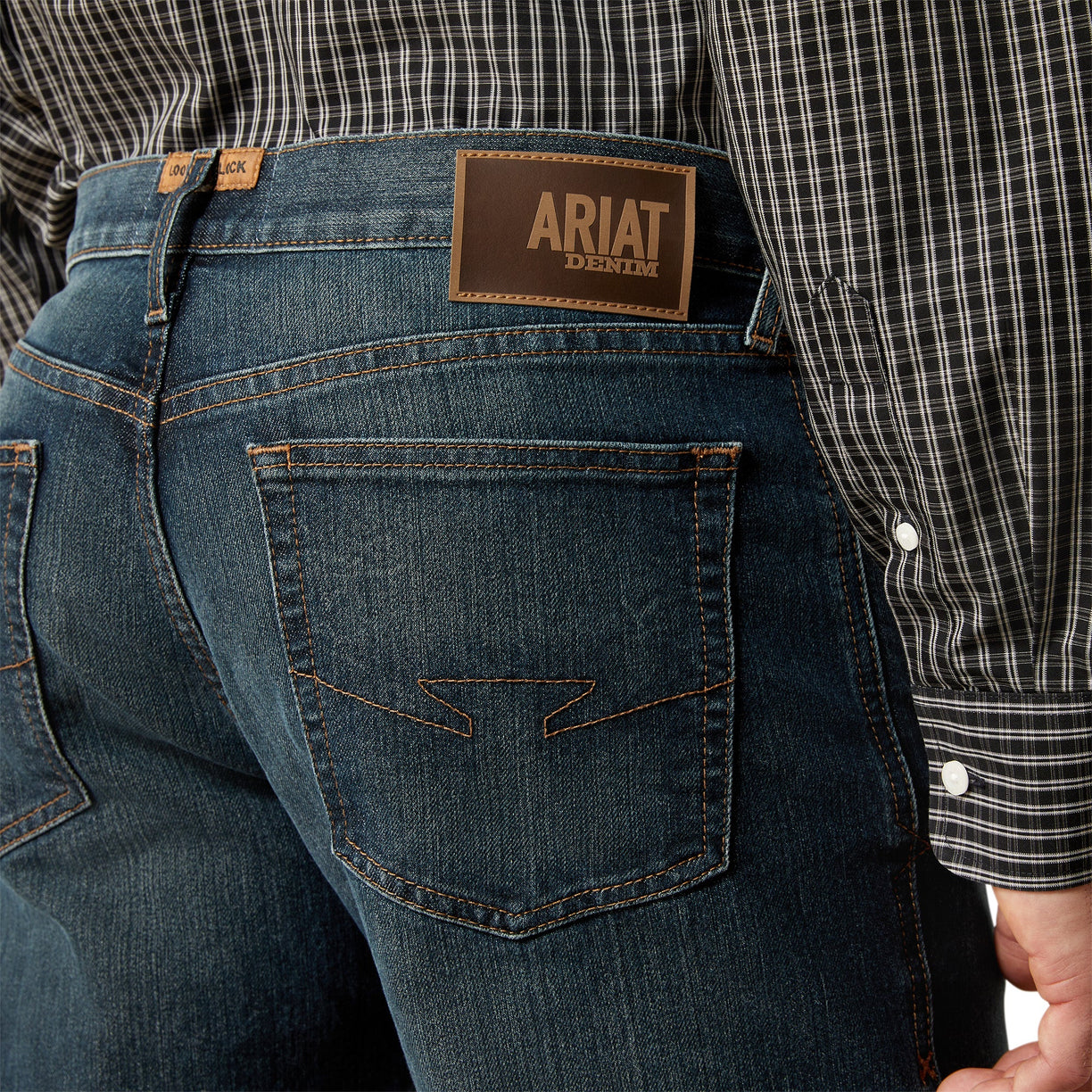 Person wearing blue jeans with Ariat denim label, plaid shirt visible