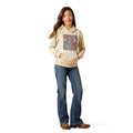 Person wearing a beige hoodie with graphic design and blue jeans on a white background