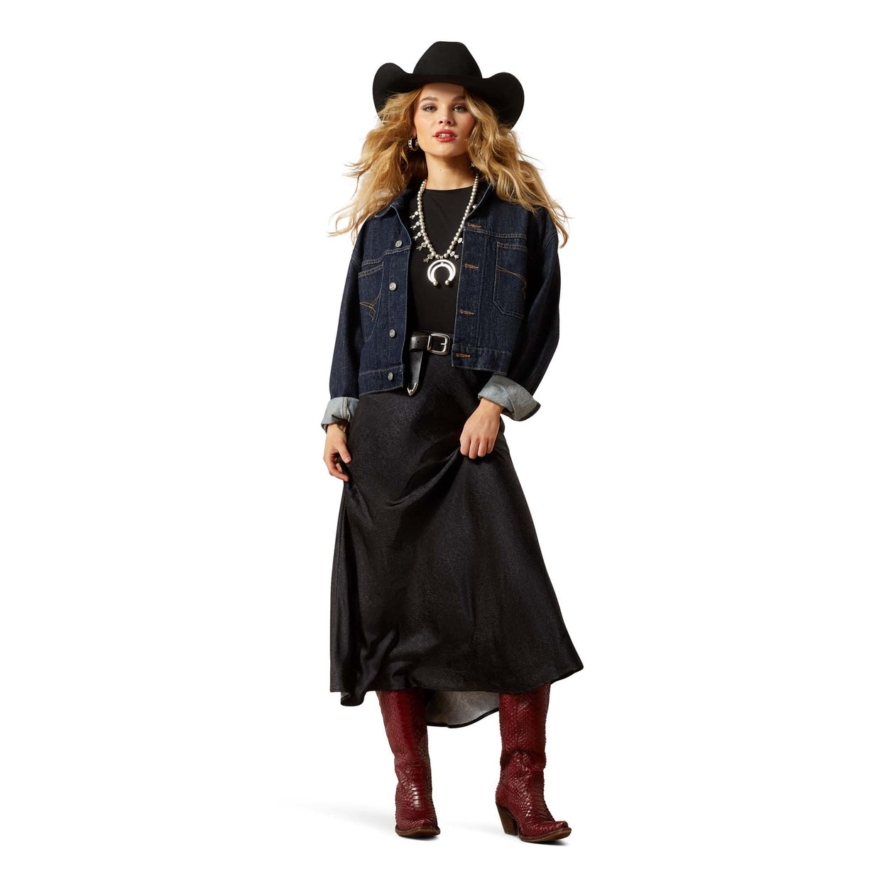 Woman wearing a denim jacket, black dress, red boots, and cowboy hat on a white background