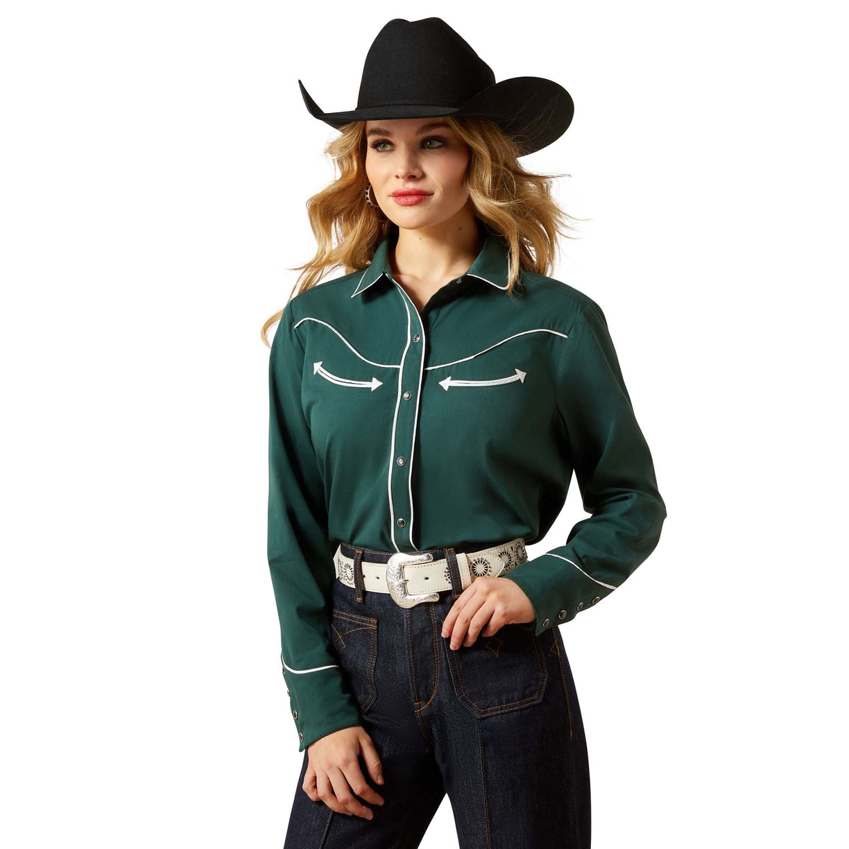 Woman wearing a green cowboy shirt with white stitching, black cowboy hat, and dark jeans on a beige background.