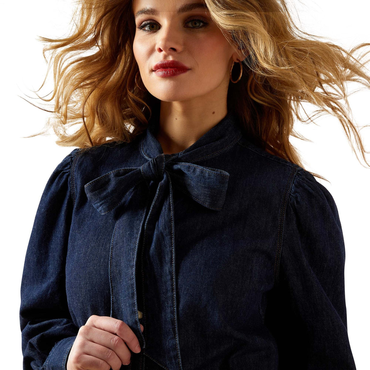 Woman wearing a dark blue coat with a bow detail on a white background