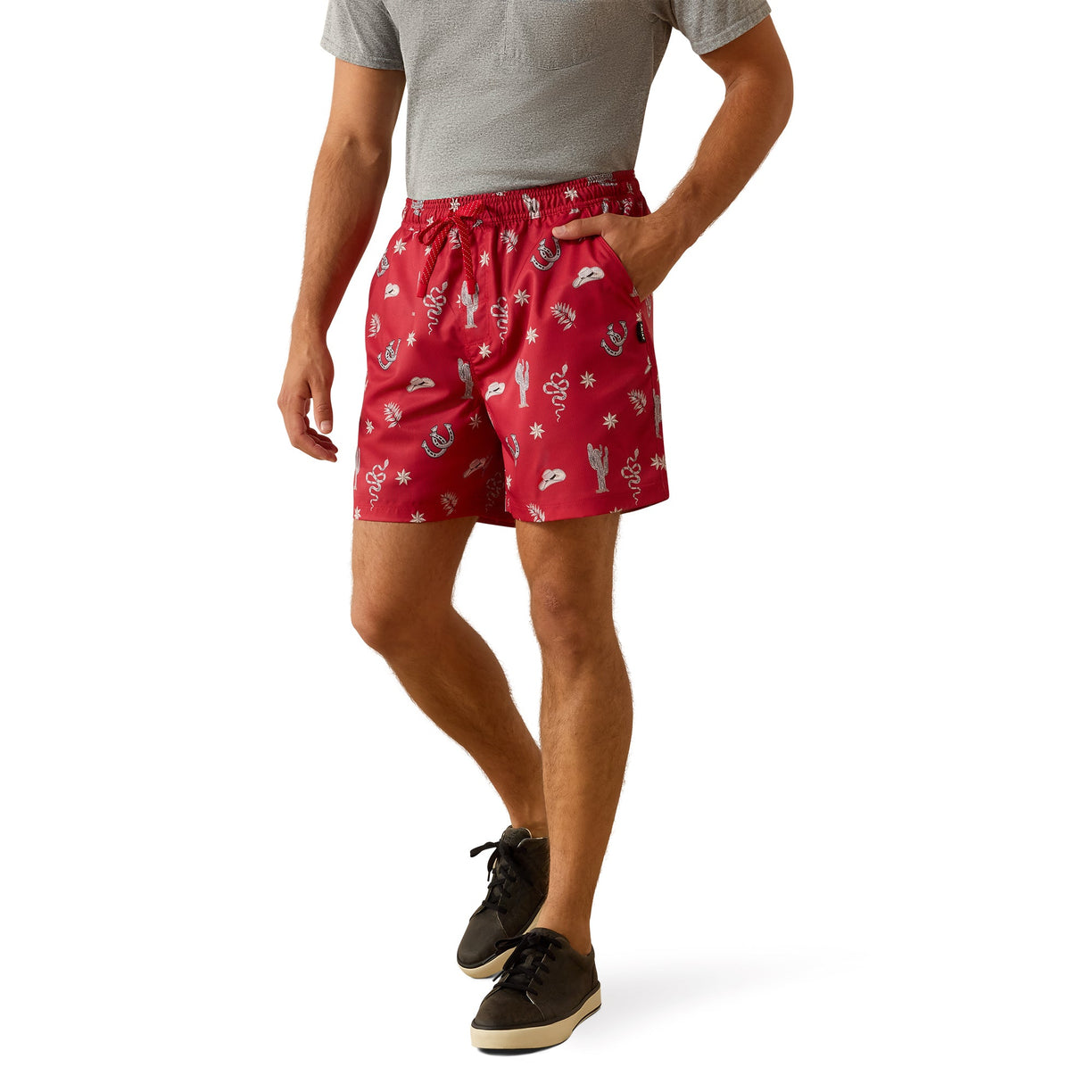 A man wearing red drawstring shorts with a white printed pattern, paired with a gray t-shirt and black sneakers, shown from the waist down on a white background.