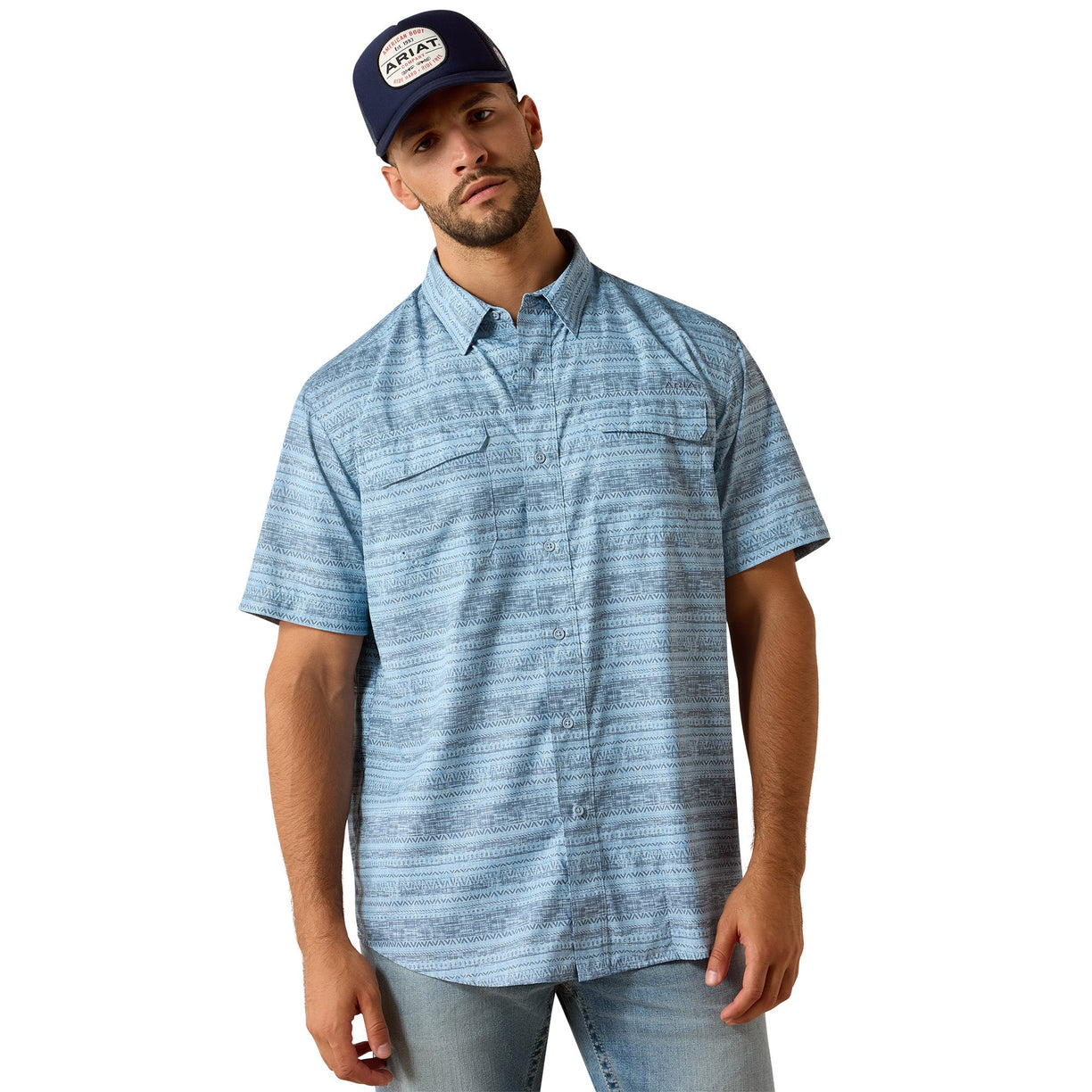 Light blue heathered shirt with a subtle geometric print, short-sleeve with dual chest pockets, styled with a cap and denim.