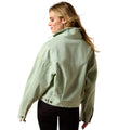 A woman shown from the back wearing a light sage green cropped jacket with a high collar and black pants, photographed against a solid white background.