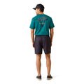 A man shown from the back wearing a teal short-sleeve t-shirt with a graphic on the back, dark charcoal shorts, and a black baseball cap, standing against a plain white background.