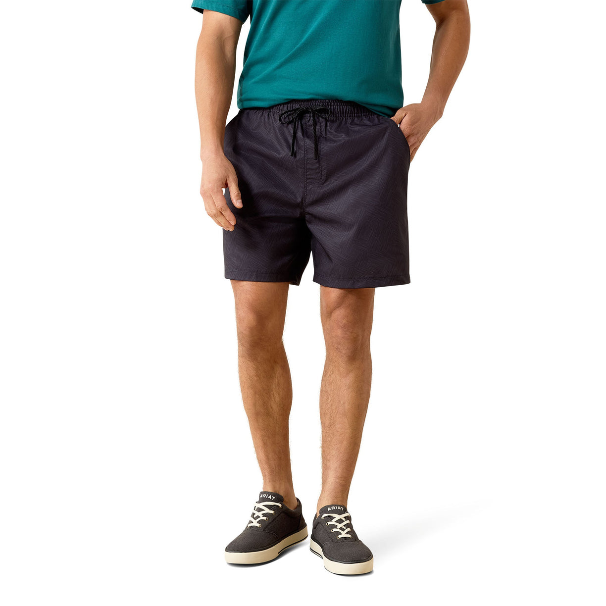A man wearing dark navy drawstring shorts, a teal t-shirt, and dark gray sneakers, standing against a white studio background.