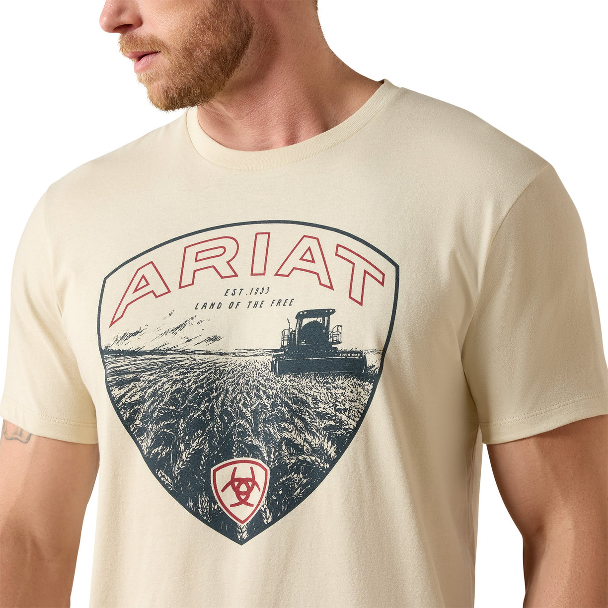 Man wearing a cream-colored t-shirt with Ariat logo and tractor graphic