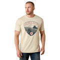 Man wearing a beige t-shirt with Ariat logo and graphic design on a white background