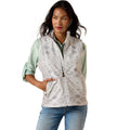 A woman modeling a sleeveless zip-front vest with a light gray and white geometric pattern, worn over a sage green shirt and blue jeans against a plain white background.