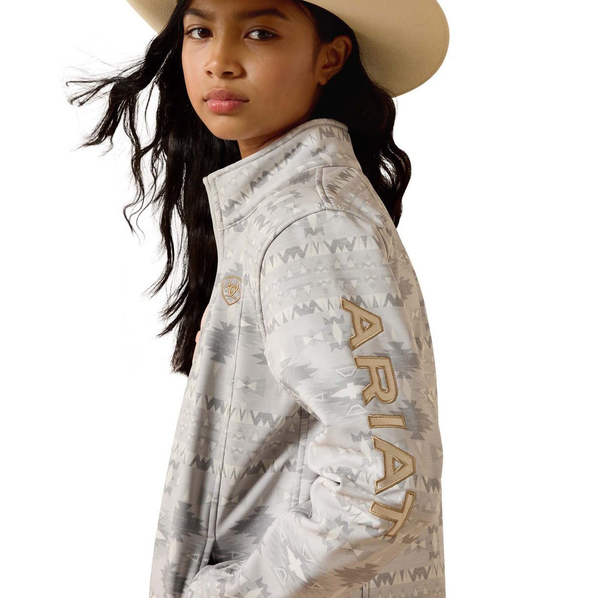A girl wearing a light gray and white patterned Ariat jacket, a cream cowboy hat, and dark hair, shown in a side profile against a white background.