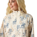 Woman wearing a cream-colored jacket with blue horse and rider pattern on a white background