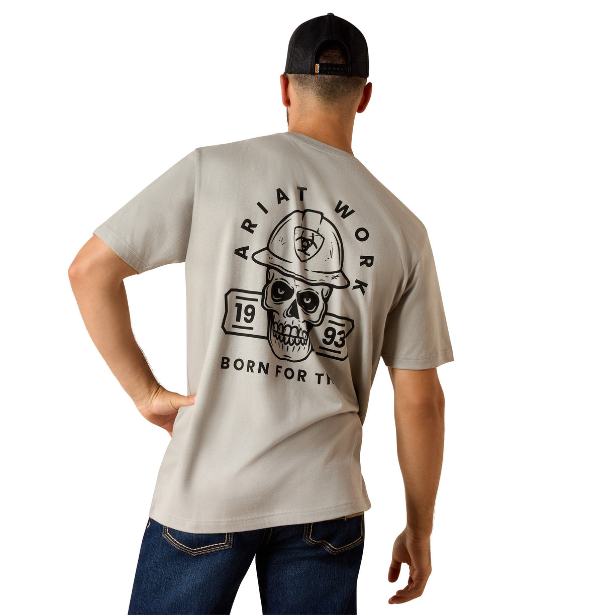 Tan graphic t-shirt with a skull and hard hat print across the back, paired with denim jeans